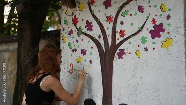 Fototapeta A woman paints a public autism awareness mural. The symbol of autism.