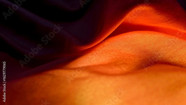 Obraz Close-up view of flowing orange and dark fabric with soft folds.