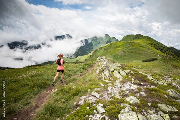 Obraz młoda kobieta biegnie samotnie na ekstremalnych przygodach ultra trail z wysokogórską scenerią i błękitnym niebem