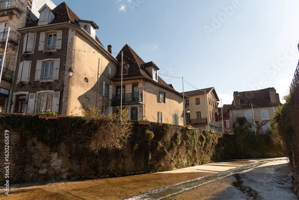 Fototapeta View of the impressive medieval architecture of the small stone houses by a river in the touristic southern French village of Sales de Bearn at sunset.
