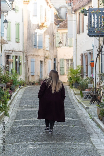 Fototapeta Vertical image of a woman strolling through the picturesque village of Salies-de-Béarn in southern France, taking in the charm of its vibrant, colorful façades and quaint architecture