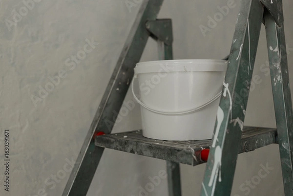Fototapeta Plastic jar with white wall paint on a stepladder. Process of painting walls in a room