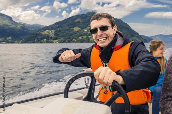 Fototapeta Portrait of young and cheerful man close up driving the motorboat, Norway. He is enjoying the moment.