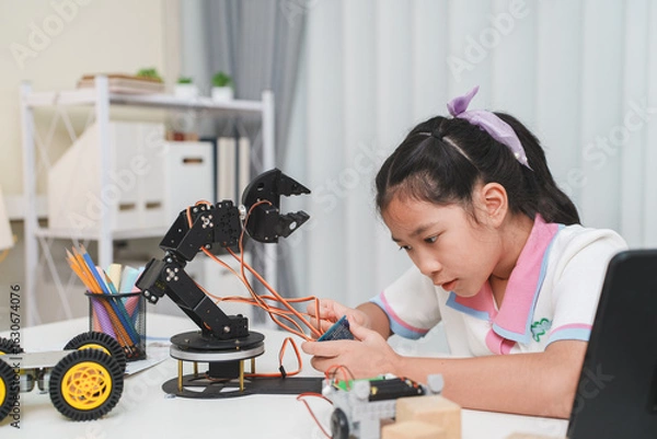 Fototapeta A young girl builds a robot, learning science and technology. STEM education concept.