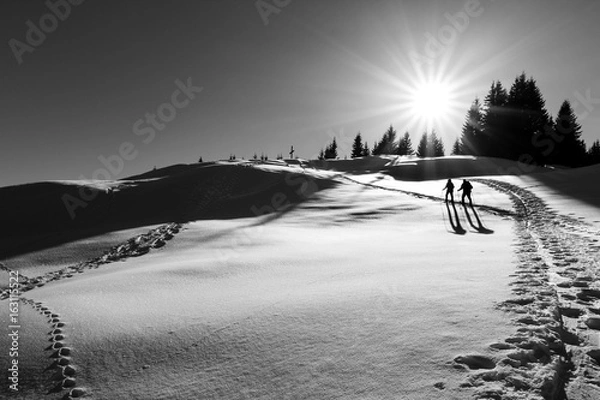 Obraz Two ski hikers walking towards summit cross with back light.