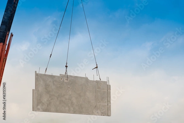 Fototapeta Construction site crane is lifting a precast concrete wall panel.
