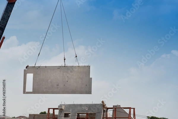 Fototapeta Construction site crane is lifting a precast concrete wall panel.