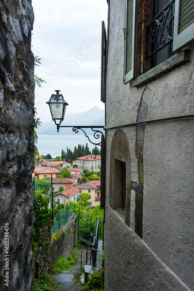 Fototapeta An old street lamp in a gap between old buildings overlooking houses with tiled roofs and Como Lake, Lombardia, Italy