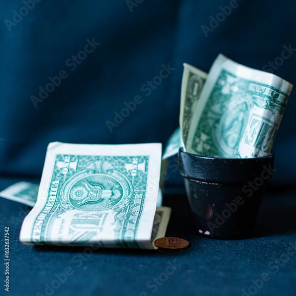 Fototapeta Several one dollar bills in and around a black tip jar. The photograph is situated on a black background using studio lighting. 