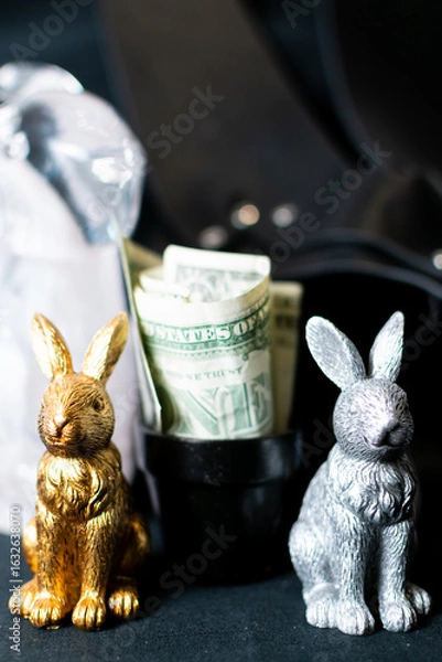 Fototapeta Two metal statues of rabbits and a glass sculpture of a rabbit surrounding money within a triangular positioning. 