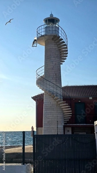 Fototapeta photo of a car standing on the seashore, a seagull flying over it, bird, building, lighthouse, summer, vacation, spiral staircase