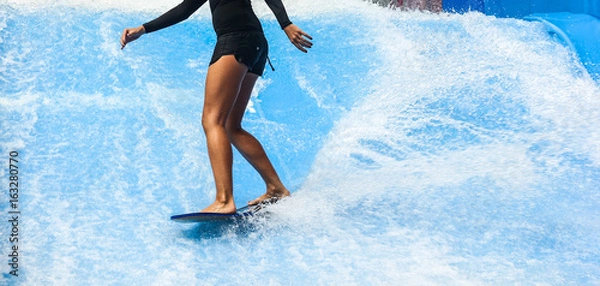 Fototapeta Dziewczyna na czarnym stroju kąpielowym surfing na basenie z falami z małą deską na wyspie Phuket, Tajlandia