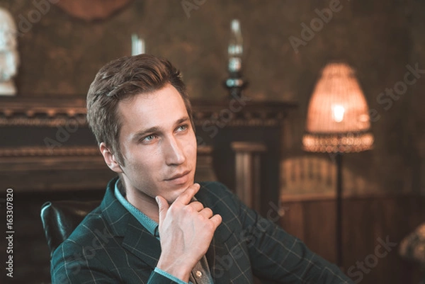 Obraz Portrait of a business man who sits by the fireplace with a thoughtful look...