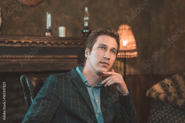 Obraz Portrait of a business man who sits by the fireplace with a thoughtful look...