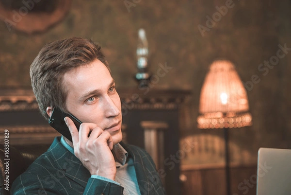 Obraz Man with computer sitting by the fireplace and talking on the phone