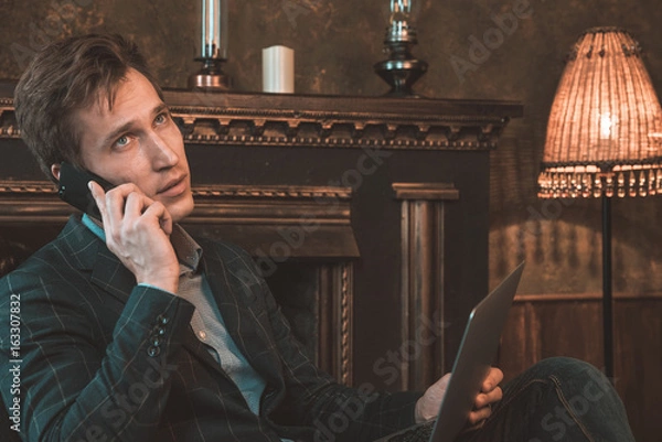 Obraz Man with computer sitting by the fireplace and talking on the phone