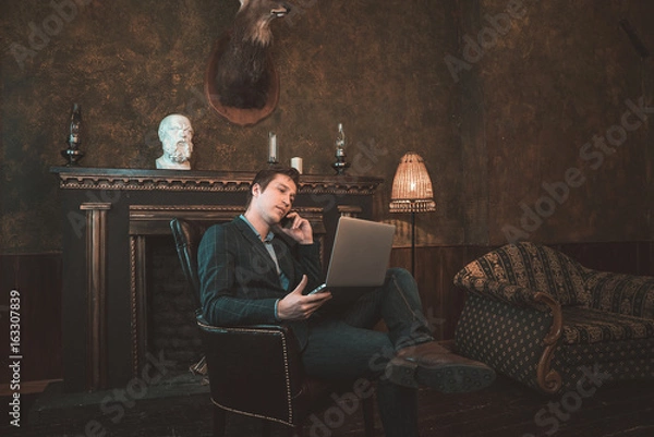 Obraz Man with computer sitting by the fireplace and talking on the phone