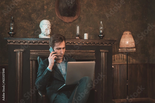 Obraz Man with computer sitting by the fireplace and talking on the phone