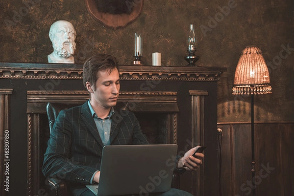 Obraz Man with computer sitting by the fireplace and talking on the phone