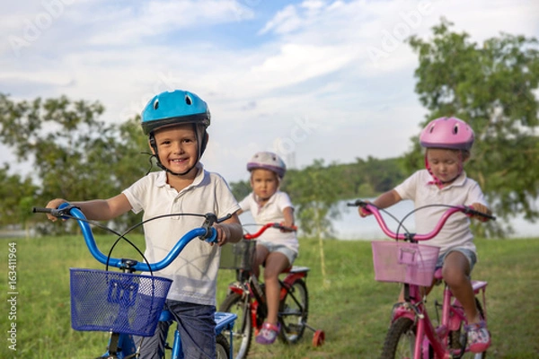 Obraz Three child riding a bicycle. The kids in a helmet riding a bike in the park. Beautiful kids. Close up
