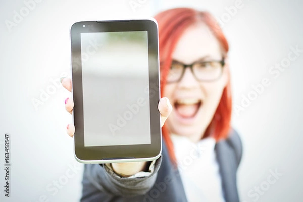 Fototapeta Business concept of success and negotiation. A woman boss, in a suit and glasses, emotionally shows the tablet. With a place for advertising text. Chef Day, Boss Day
