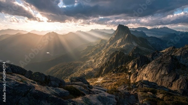 Fototapeta Breathtaking mountain landscape with dramatic clouds and sunlight rays illuminating the rocky terrain.