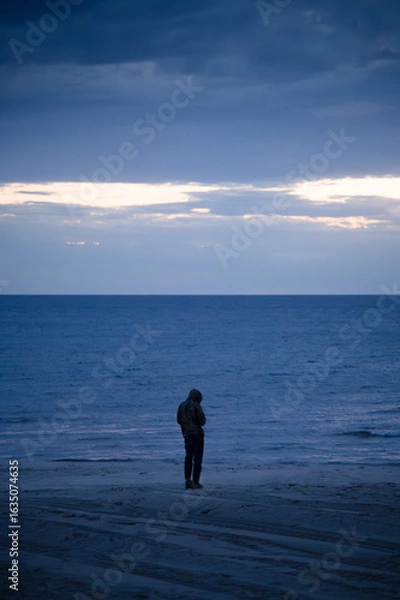 Fototapeta A person standing on the shore of Lake Michigan on a cloudy evening just after sunset