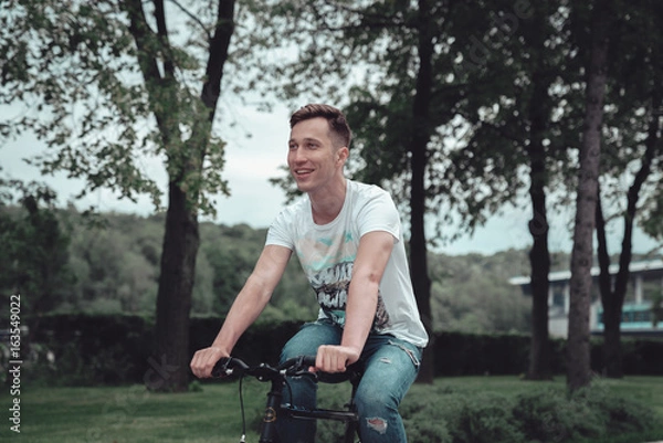 Obraz A man is riding a bicycle in a park on the waterfront