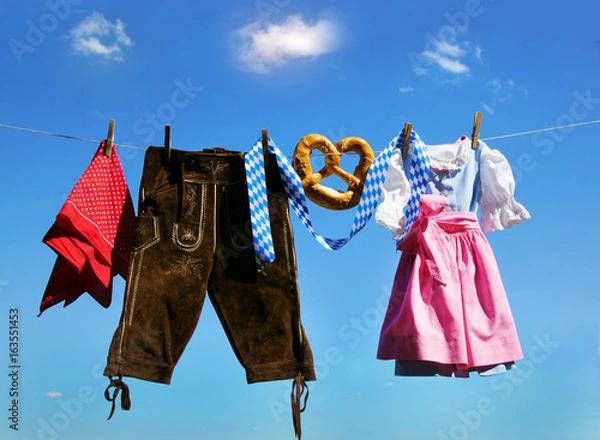 Fototapeta Fair, Oktoberfest, Volksfest, Dirndl und Lederhose hängen an Leine vor weiß-blauem Himmel, Copyspace, Textraum