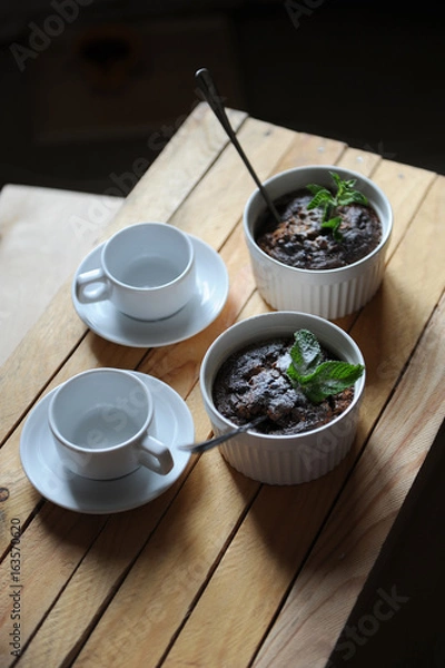 Fototapeta Healthy breakfast of oat pudding in white keraimic mold. Decorated with sprig of mint and powdered sugar. Two empty cups