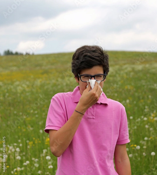 Fototapeta Allergic boy with glasses blows his nose using a white handkerch