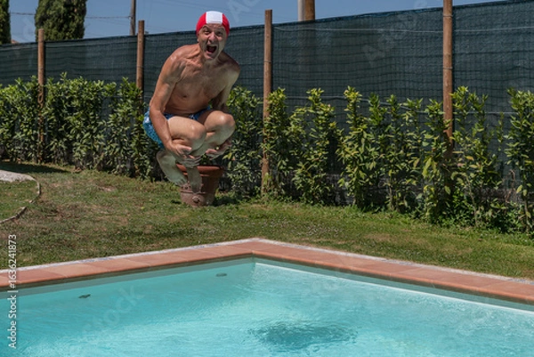 Fototapeta A man dives into a swimming pool wearing a red and white swimming cap