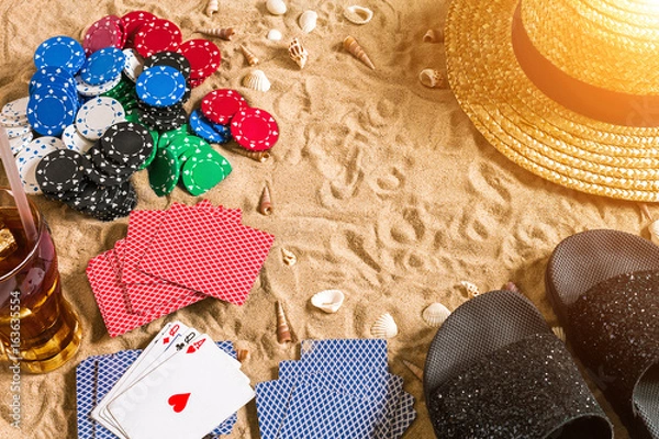 Fototapeta Beachpoker. Chips and cards on the sand. Around the seashells, hat and flip flops. Top view