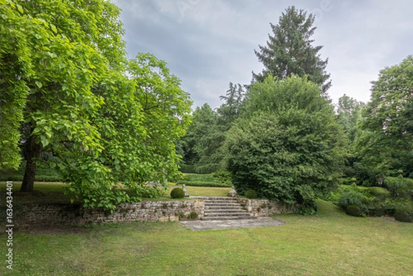 Fototapeta Lush garden with stone steps under cloudy sky