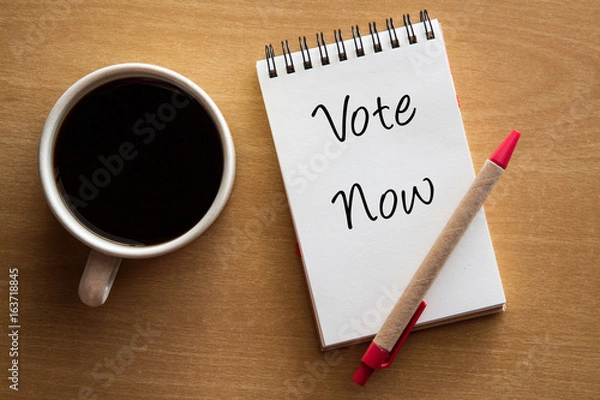 Fototapeta Vote now handwriting on notebook with cup of coffee.