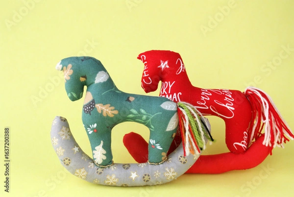 Fototapeta Two Tilda-style horses sewn from fabric. Concept - Christmas toy, Christmas tree decoration, New Year theme. Yellow background, horizontal photo. There is space for text.