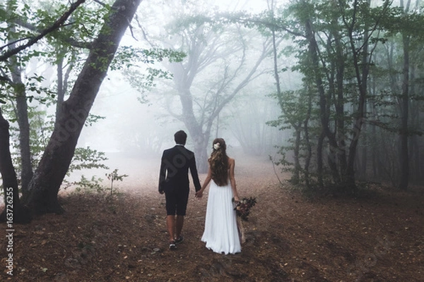 Fototapeta Bride and groom walking in autumn forest. Amazing autumn fog and  mystery mood. Beautiful nature around