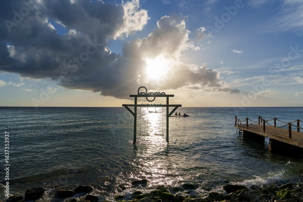 Obraz Pier de madeira no Caribe em Curaçao ao pôr do sol, com raios de luz refletindo no mar calmo e cenário tropical sereno, ideal para transmitir paz e beleza natural