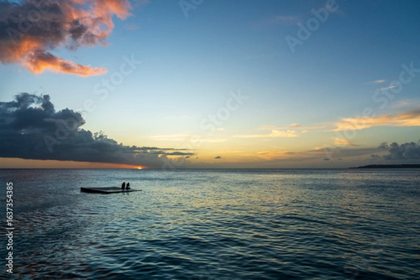 Obraz Crianças brincando em plataforma flutuante no mar do Caribe ao pôr do sol em Curaçao, capturando momentos de diversão, liberdade e beleza tropical.