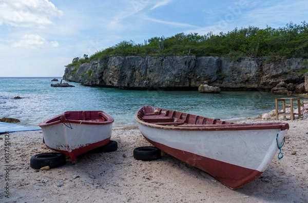 Obraz Two traditional fishing boats on a sandy Caribbean beach in Curaçao, with turquoise waters and rocky cliffs, capturing tropical charm, coastal lifestyle, and serene island vibes.