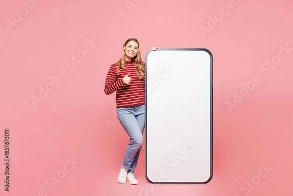 Fototapeta Full body young happy woman she wearing red striped sweatshirt casual clothes big huge blank screen mobile cell phone smartphone with copy space area show thumb up isolated on plain pink background.