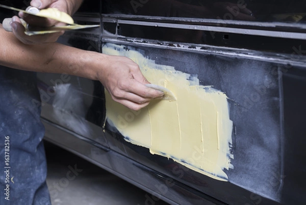 Fototapeta Auto body repair series: Mechanic applying putty filler