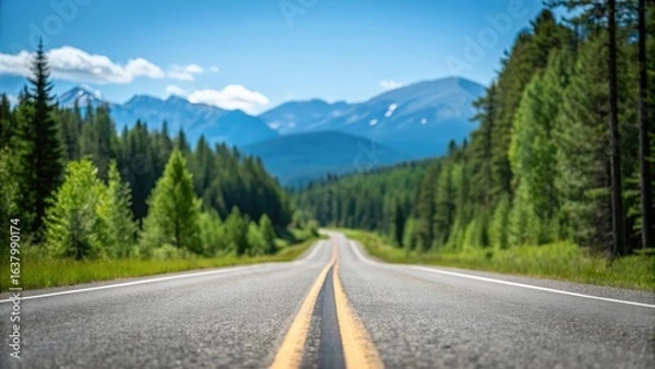 Fototapeta Asphalt highway stretching through lush green forest — mountain landscape under clear blue sky
