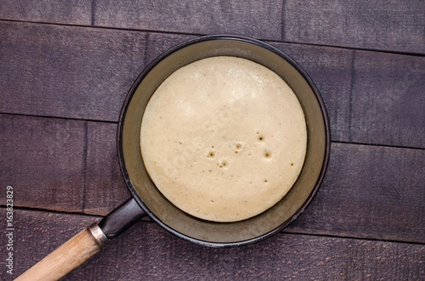 Fototapeta Raw pancake in a frying pan on a dark background