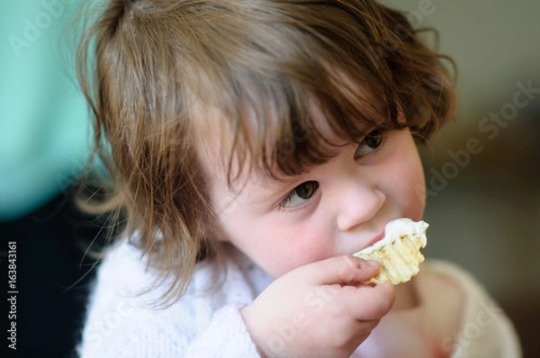 Obraz Portrait of a cute little girl inside eating potato chip with sour cream dip on it