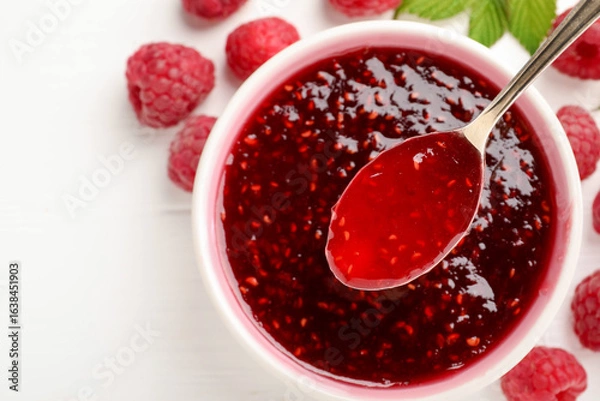 Fototapeta Sweet raspberry jam in bowl, berries and green leaves on white table, flat lay. Space for text