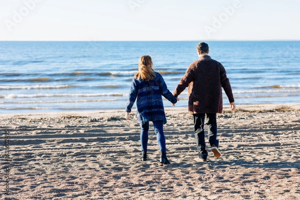 Obraz Loving couple walks on beach along sea on sunny autumn day. Weekend and lifestyle concept. Back view. High quality photo