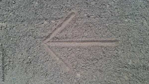 Fototapeta Arrow Sign Drawn on Sand Pointing Left, Simple Directional Symbol for Navigation, Path Guidance, Outdoor Activities, Travel Orientation, and Instructional Design Element