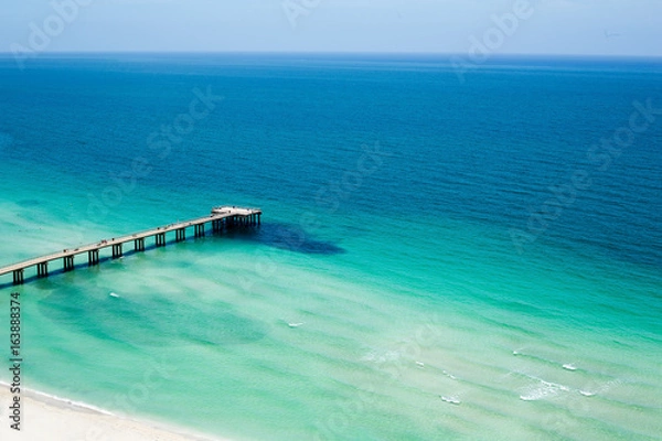 Fototapeta Pier jutting out into the ocean under clear blue skies