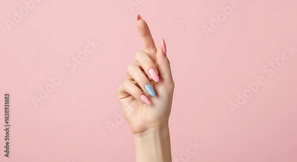 Fototapeta Elegant female hand with a trendy multicolored manicure pointing upwards, isolated on a solid pastel pink background.